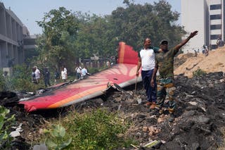 People stand near debris at the site of a plane crash near Sardar Vallabhbhai Patel International Airport in Ahmedabad, Gujarat